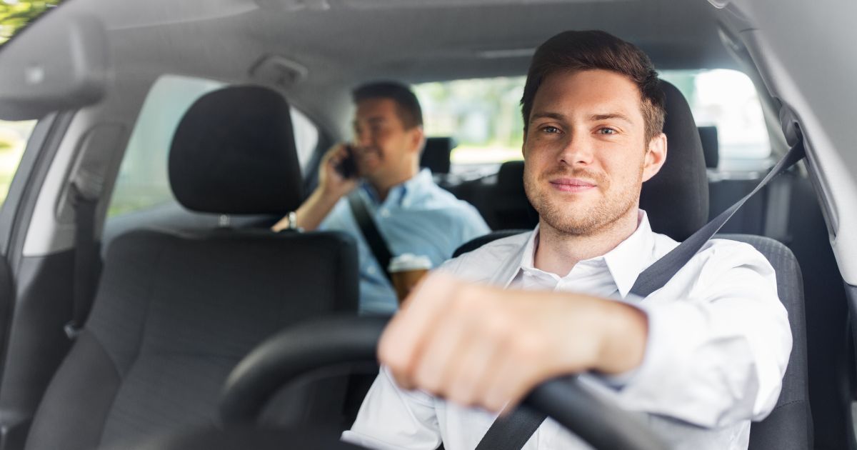 UN TASSISTA CON CAPè KB CHE SORRIDE FELICE AL CLIENTE IN AUTO